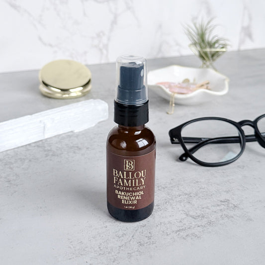 Bottle of Ballou Family Apothecary Bakuchiol Repair Elixir on a gray surface with glasses and a mirror in the background.