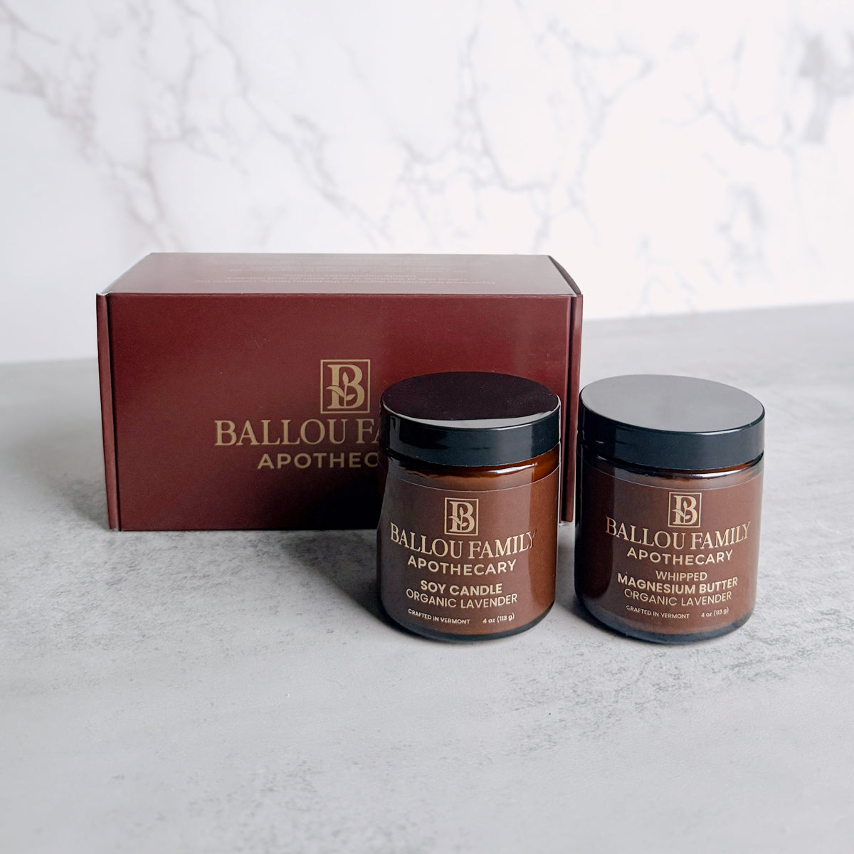 One jar of Ballou Family Apothecary Magnesium Butter and one Soy Candle with a branded box on a light background