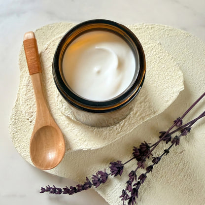 Jar of Ballou Magnesium Butter with a wooden spoon and lavender on a textured surface