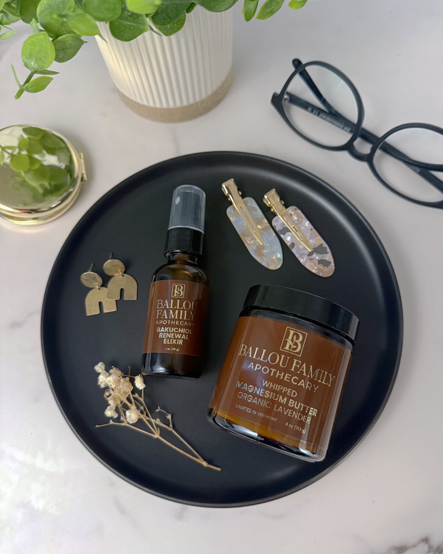 Bottle and jar of Ballou Family Apothecary on a black tray with decorative items on a white surface.