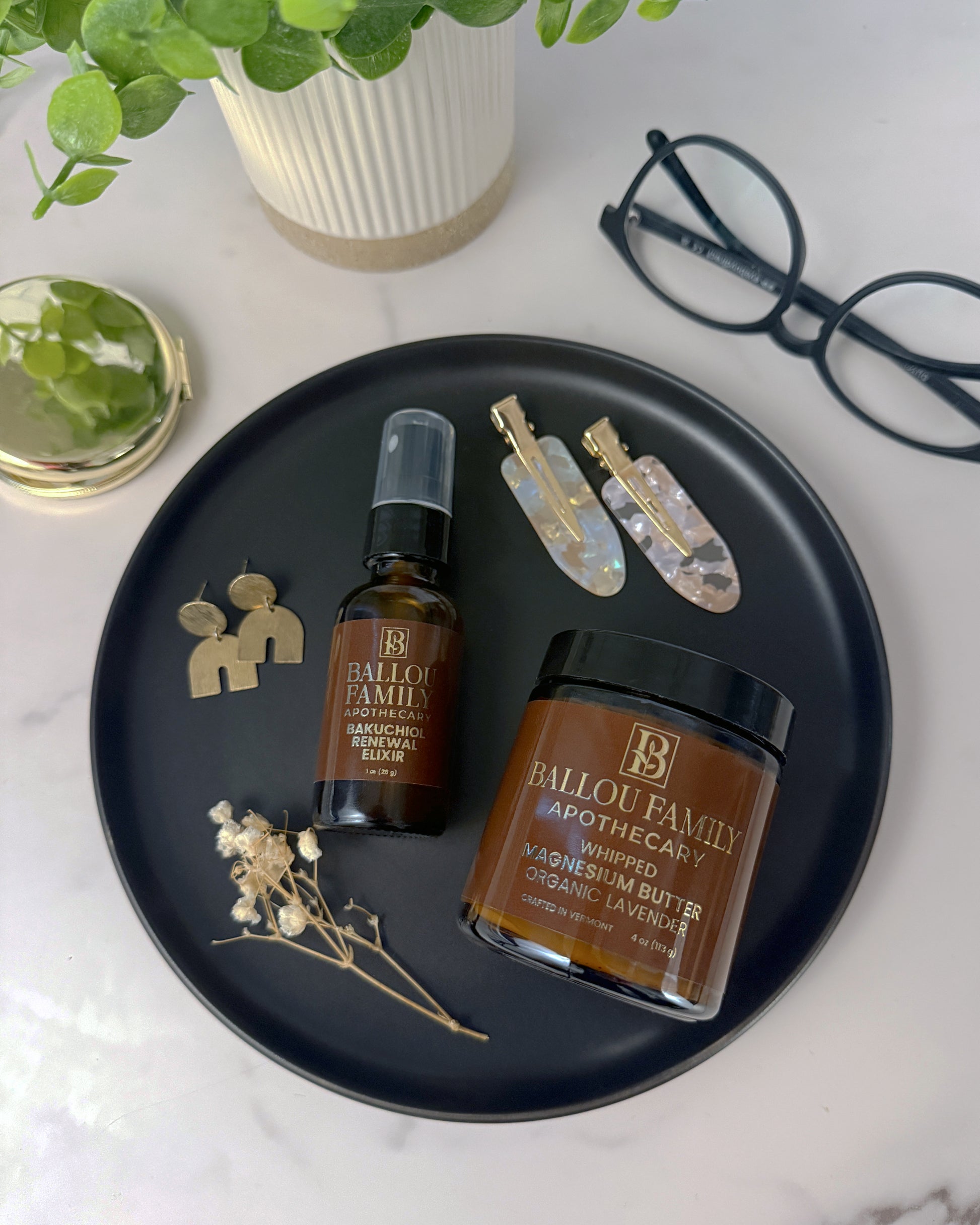 Bottle and jar of Ballou Family Apothecary on a black tray with decorative items on a white surface.