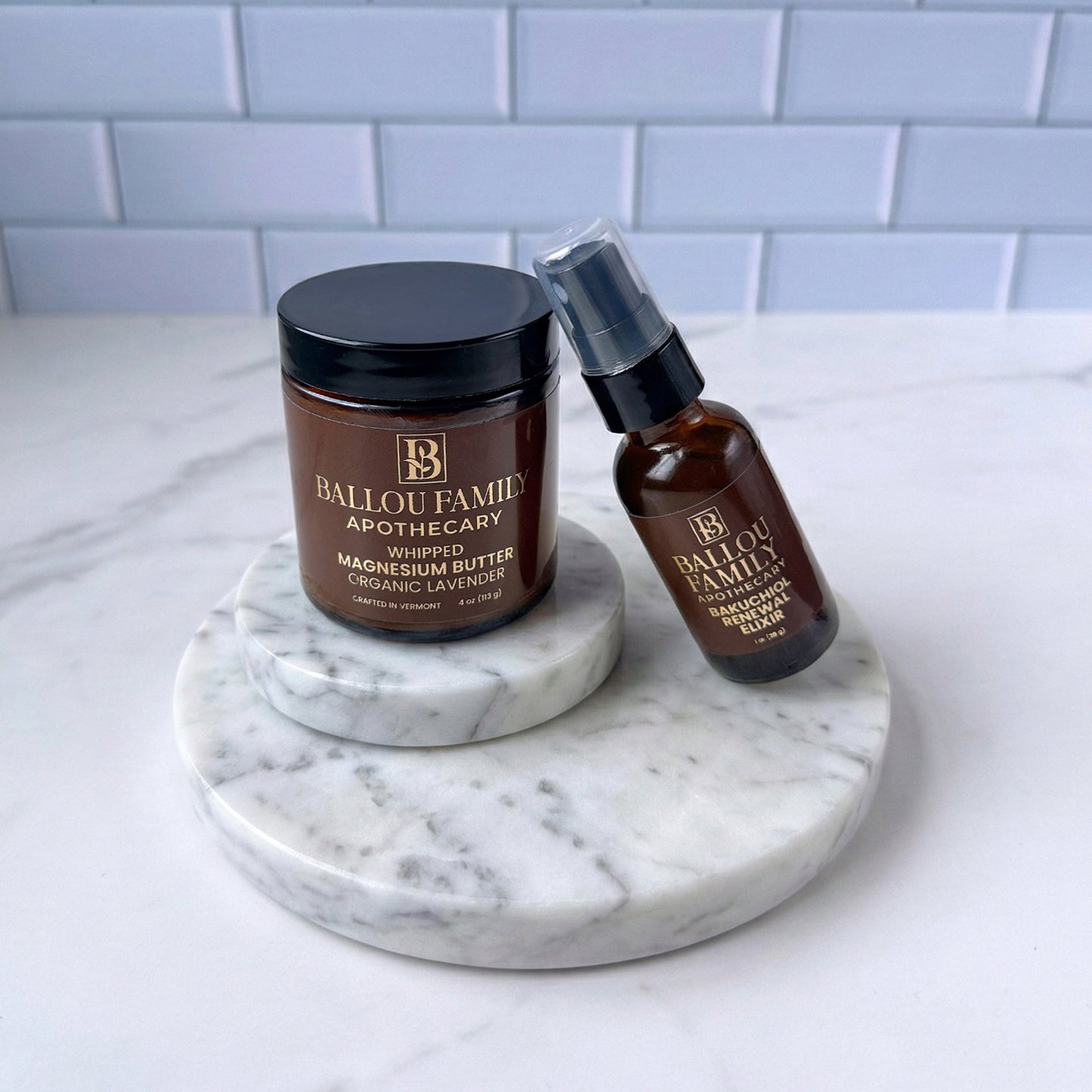 Two Ballou Family Apothecary products on a marble tray with a tiled wall background