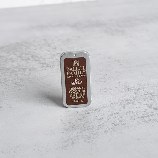 Ballou Family Apothecary organic cocoa butter lip balm tin on a gray surface
