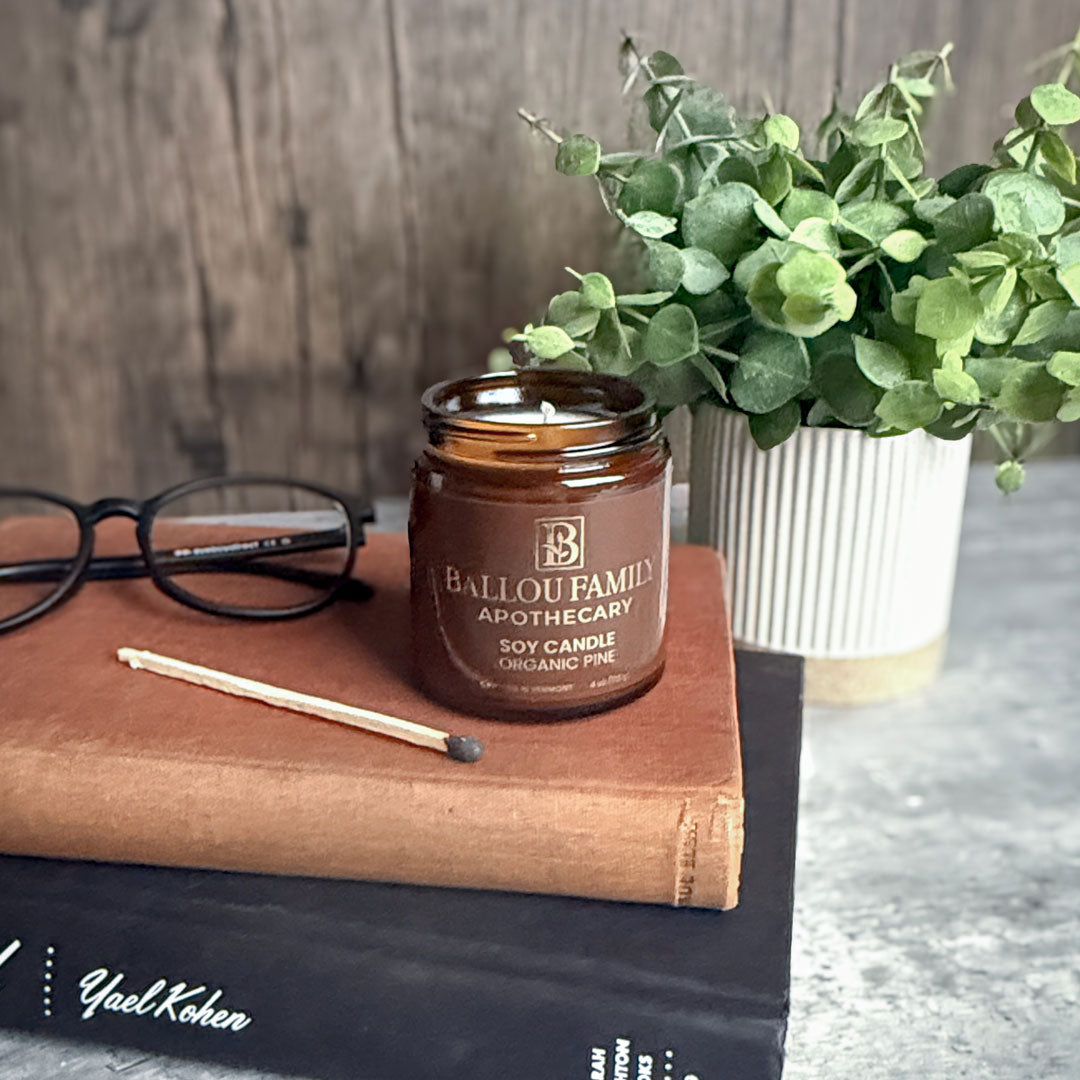 Ballou Family Apothecary soy candle on a book with glasses and a plant in the background