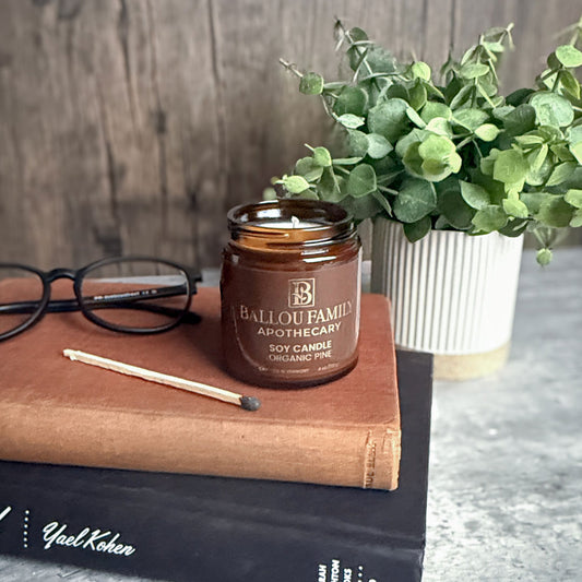 Ballou Family Apothecary soy candle on a book with glasses and a plant in the background