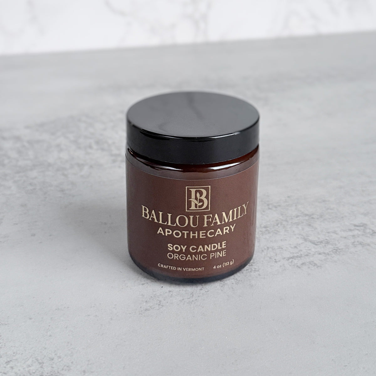 Brown candle jar with black lid on a light gray surface, featuring 'Ballou Family Apothecary' branding.