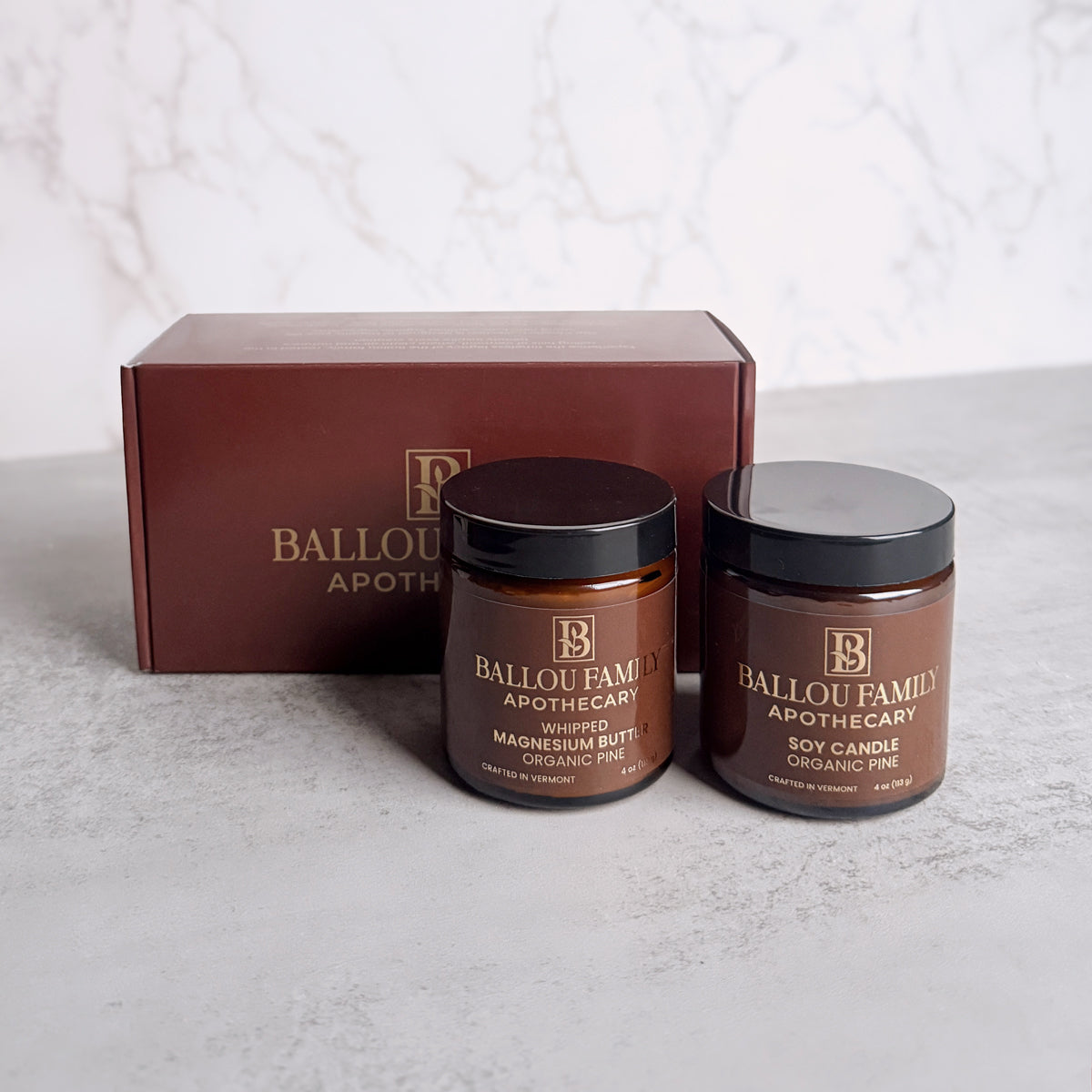 One jar of Ballou Family Apothecary Magnesium Butter and one Soy Candle with a branded box on a light background