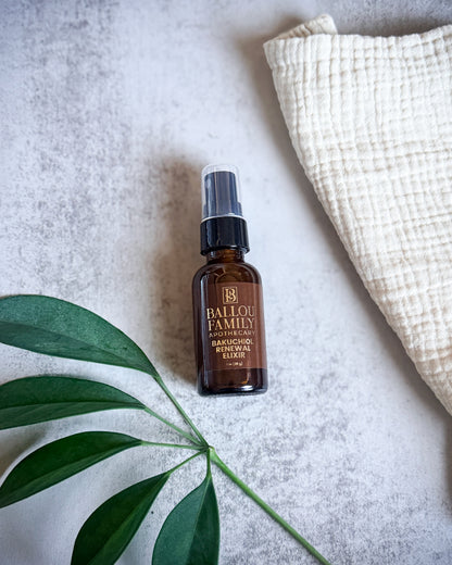 Brown bottle with black cap labeled 'Ballou Family Apothecary Bakuchiol Renewal Elixir' on a light gray surface with a green leaf and white fabric.