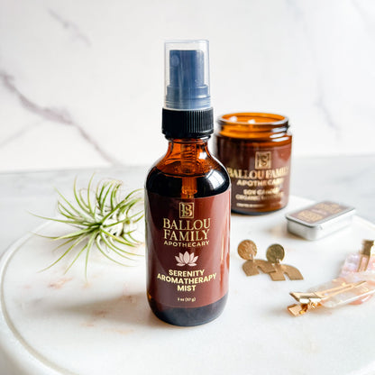 Ballou Family Apothecary Serenity Aromatherapy Mist bottle on a white surface with a jar and decorative items.