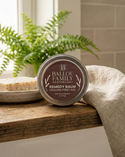 Ballou Family Apothecary Remedy Balm on a wooden surface with plants in the background